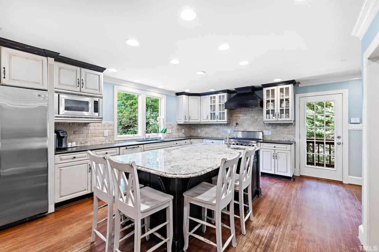 A bright, airy kitchen with light blue paint, black and white cabinetry, and gray brick backsplash